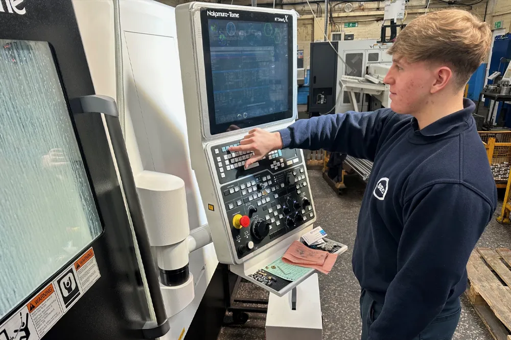 A machinist at the control of a Nakamura-Tome multi-axis lathe